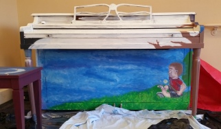 A piano with a picture of a boy sitting in grass on it.
